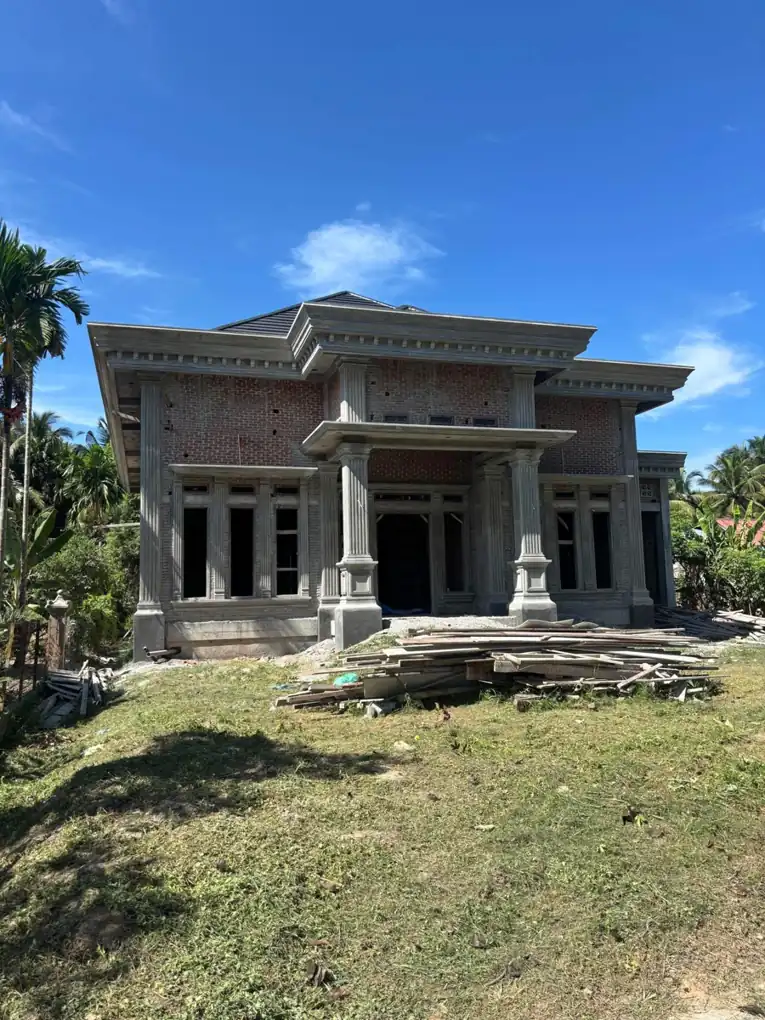 Fasad rumah dengan kolom depan dan permukaan yang belum seluruhnya selesai.