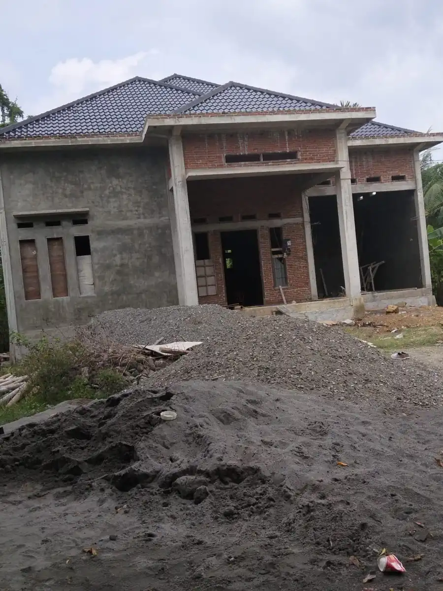 Bangunan rumah dengan dinding yang belum seluruhnya dilapisi dan area depan dalam pengerjaan.