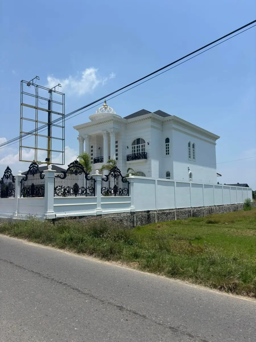 Pagar putih dengan elemen gelap di depan bangunan rumah.